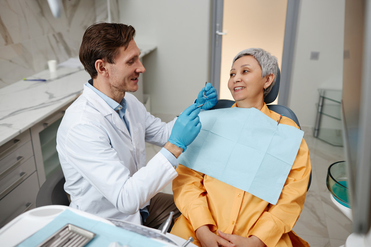 Smiling male dentist working with senior woman at office in dental clinic.