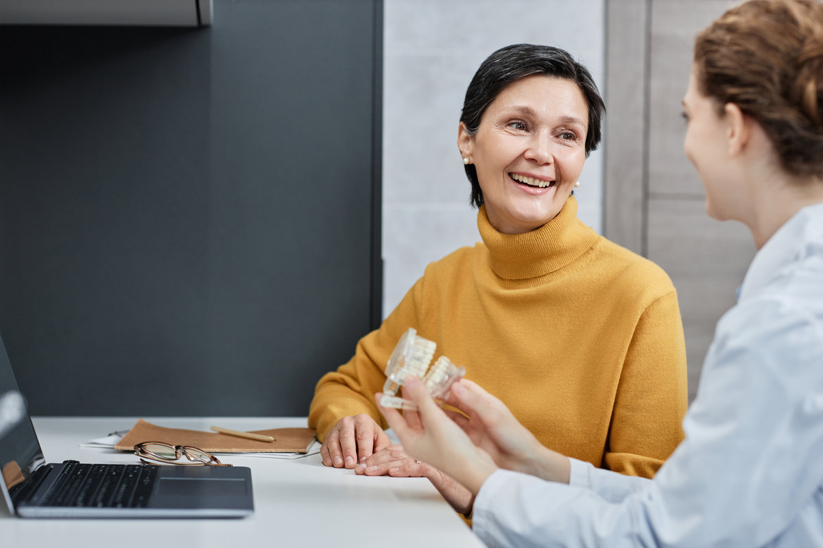 Portrait of smiling mature woman talking to dentist in dental clinic and consulting on tooth implantation, copy space